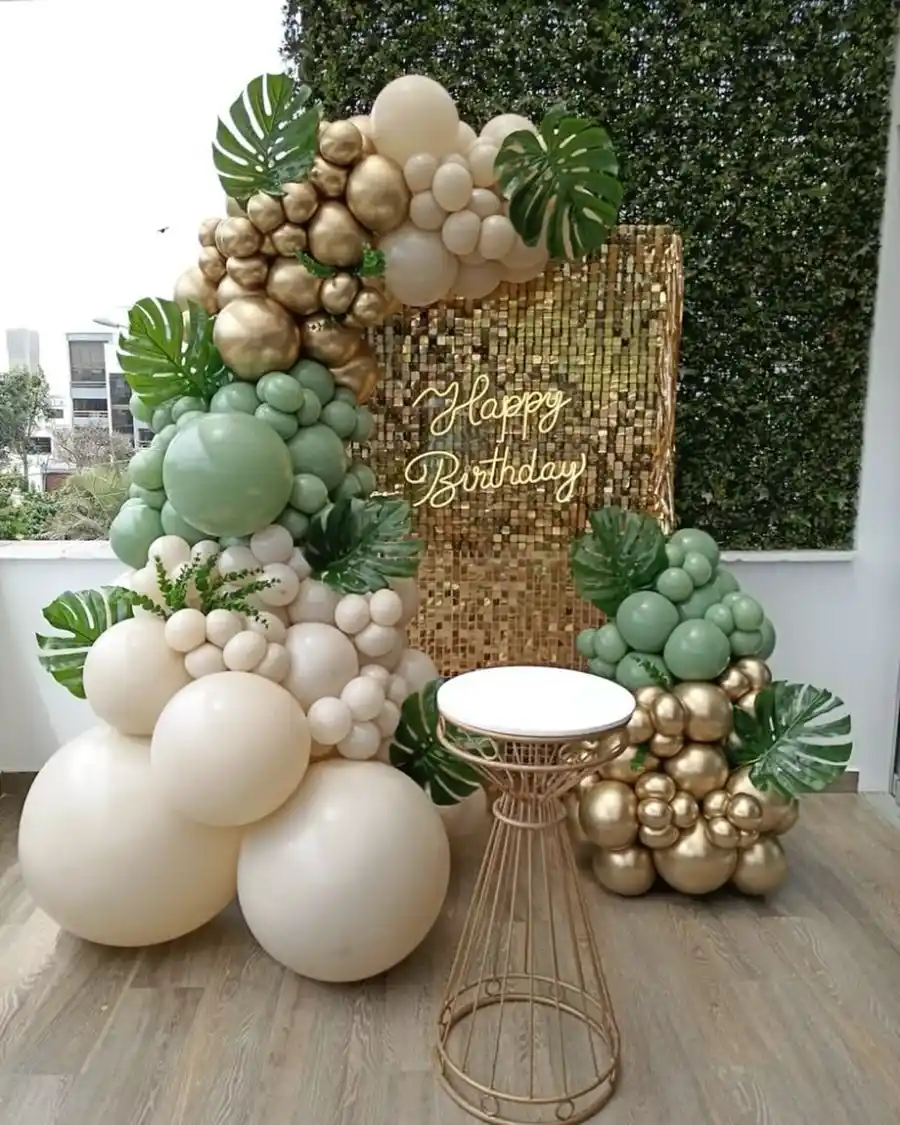 A balloon garland in sage, cream and gold beside a gold sequin wall reading Happy Birthday