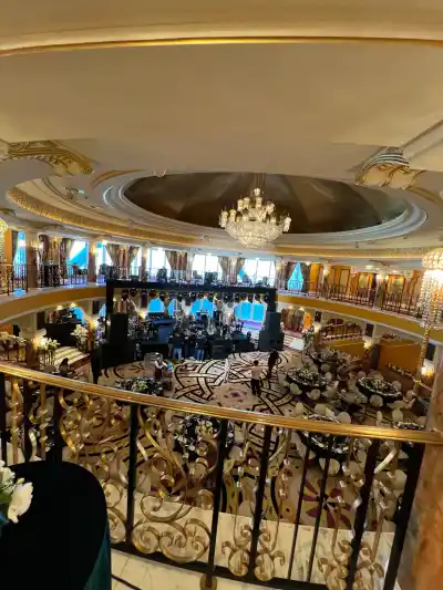 The same ballroom from the upper balcony: a chandelier under a gold leaf dome, the stage rigged and the floor set for a banquet