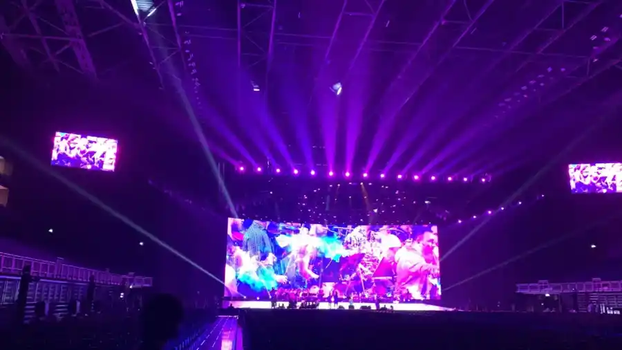 An arena stage with a full-width LED screen and purple beam lighting